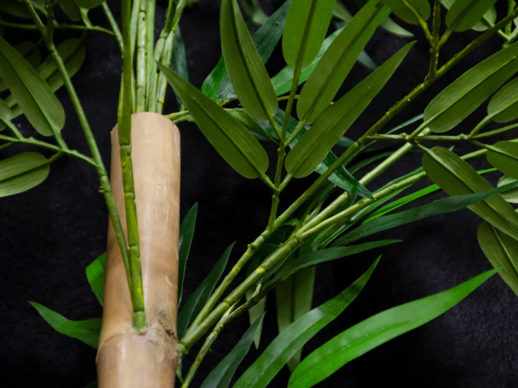 Artificial bamboo with smooth tan stalk and clusters of slender green leaves on jointed stems.