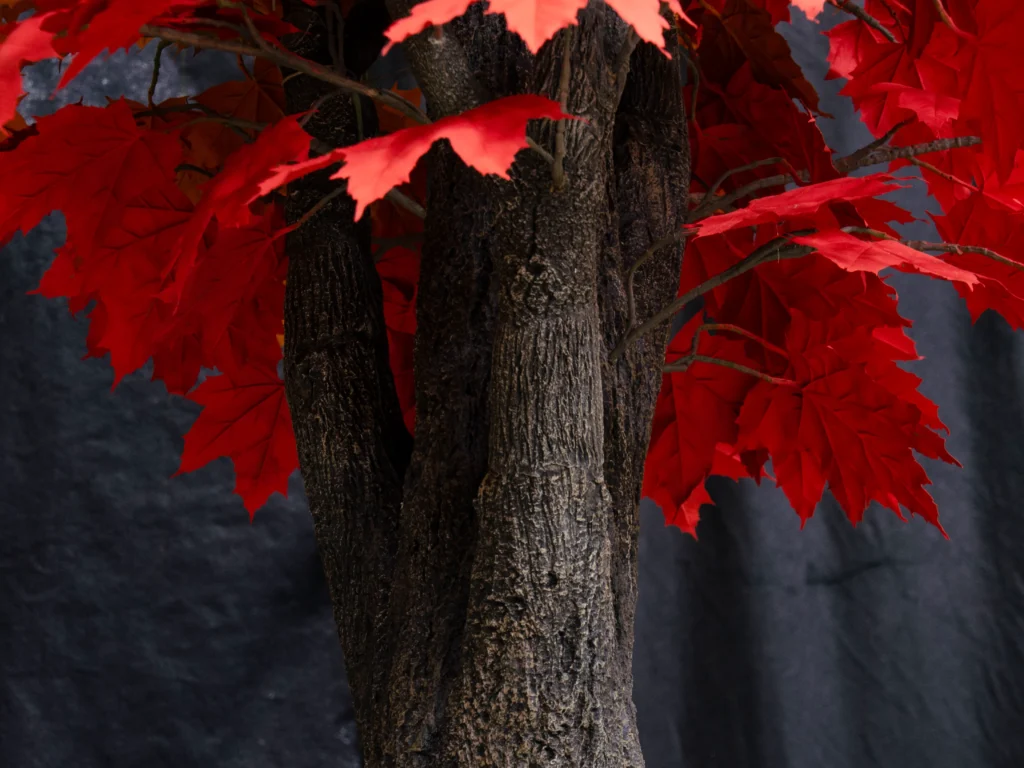 Artificial maple tree with dark textured trunk and clusters of bright red autumn leaves.