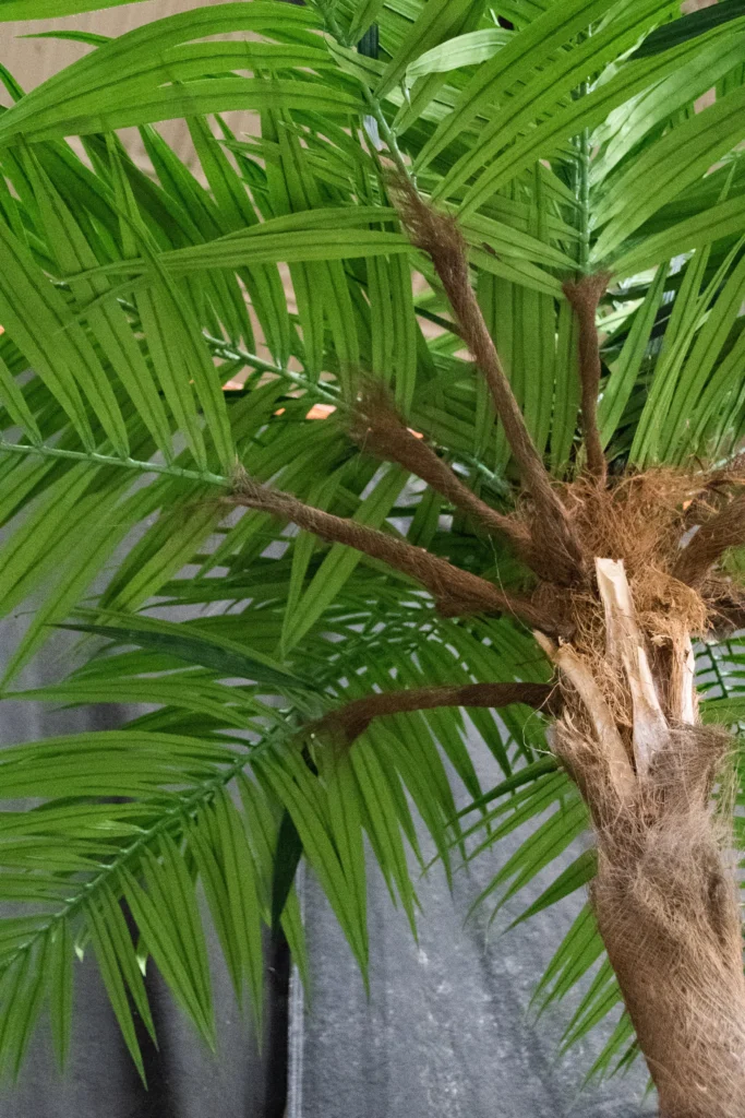 Artificial palm tree with feather-like green fronds and a textured fibrous trunk base.